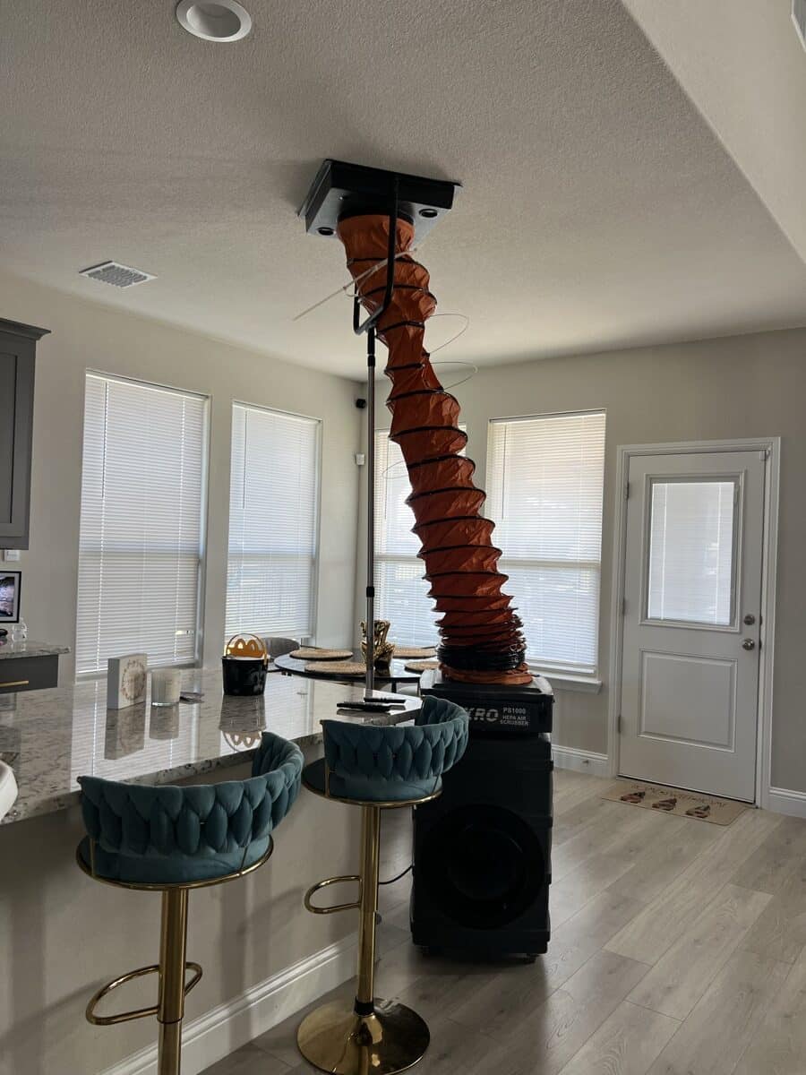 Air duct cleaning service setup with NIKRO vacuum and orange collection hose in an elegant residential living room