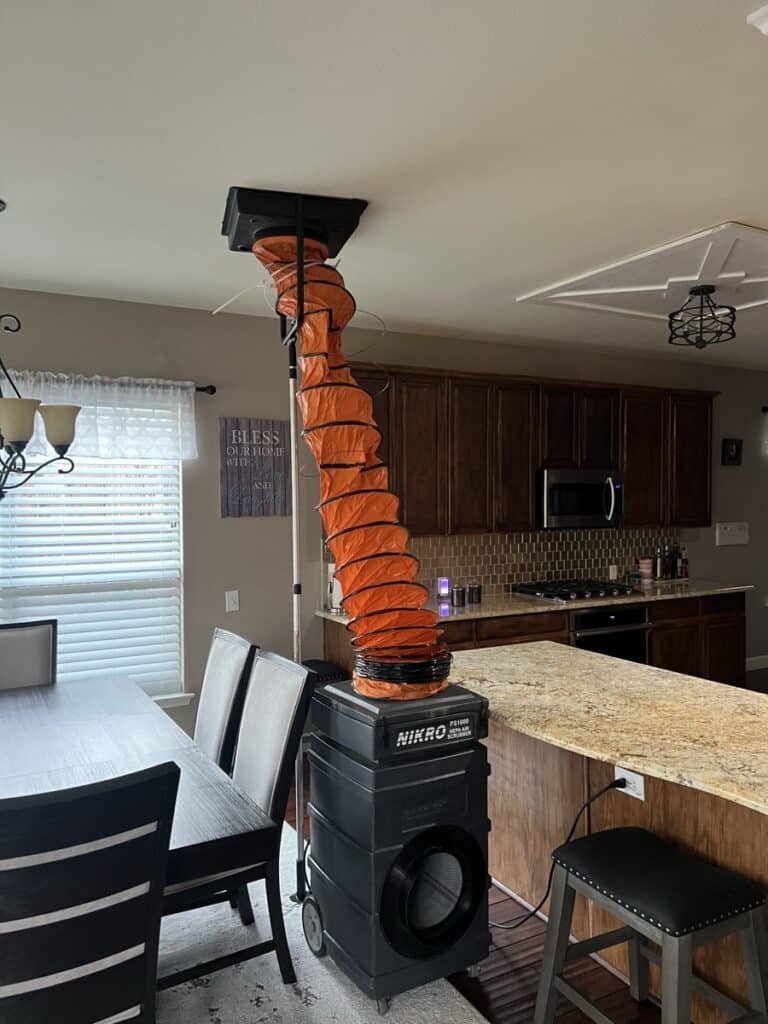 Air duct cleaning equipment set up in a spacious living room with high ceilings showing orange vacuum hose