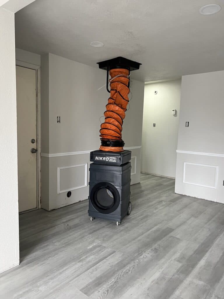 NIKRO PS1000 air duct cleaning vacuum system with orange flex hose connected to ceiling vent in customer home