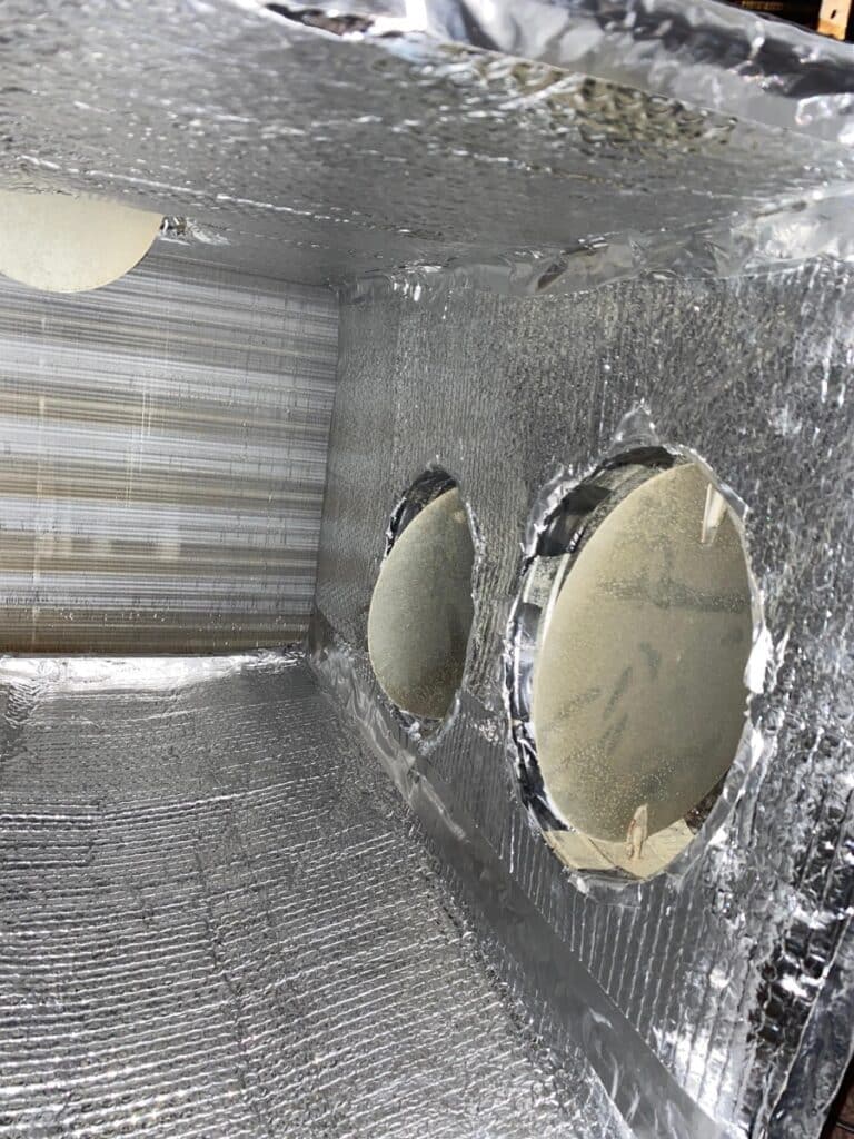 Interior view of clean plenum box showing circular duct openings and reflective insulation