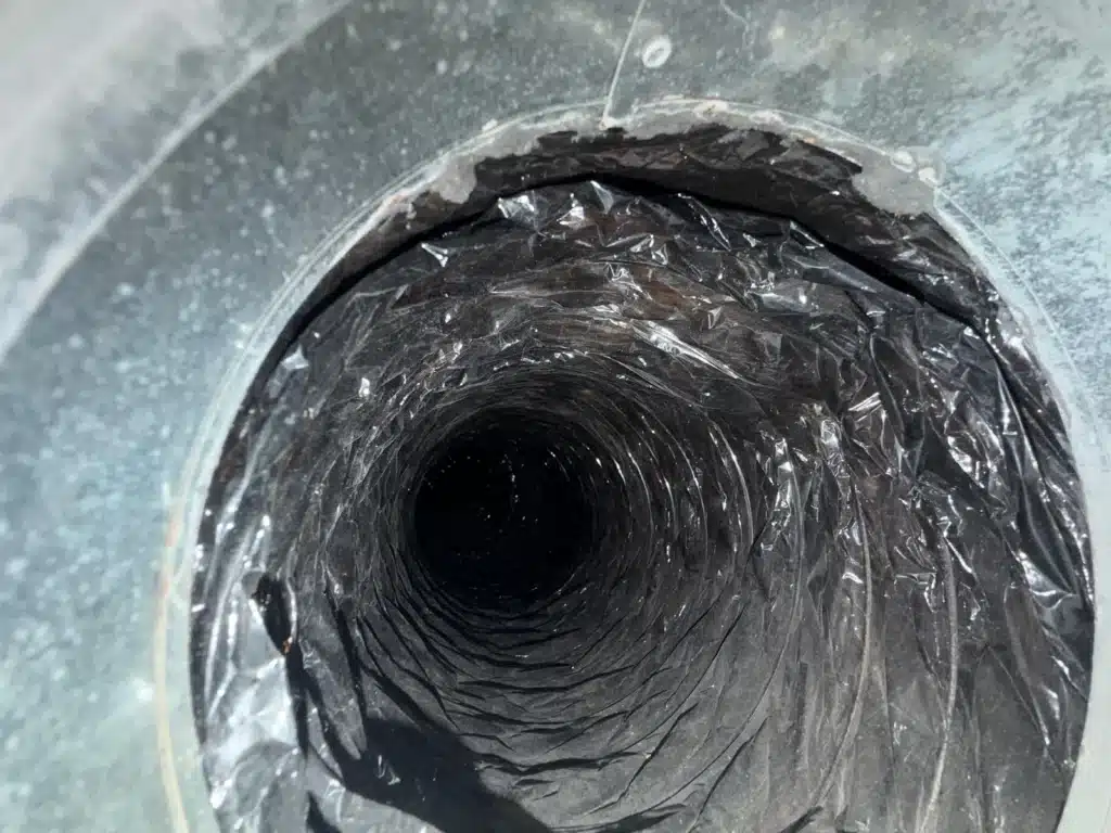 Air duct cleaning: looking into a flex duct line through its metal collar, dark inner lining exposed