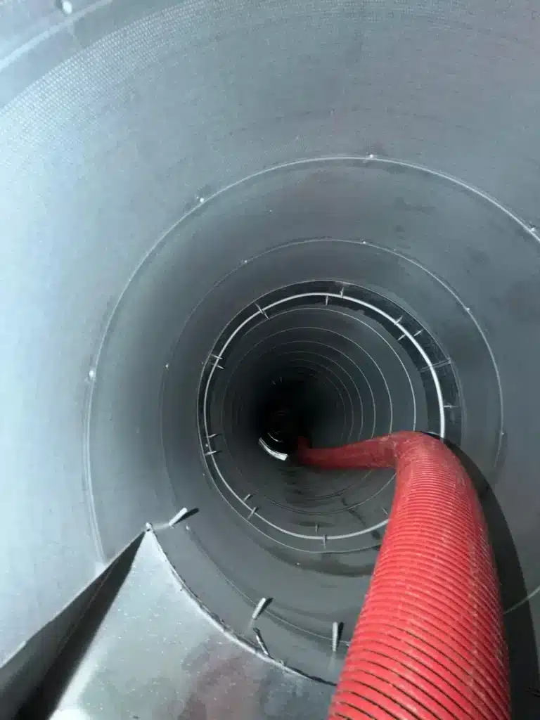 Air duct cleaning: red vacuum hose feeding into a clean sheet metal plenum and round duct