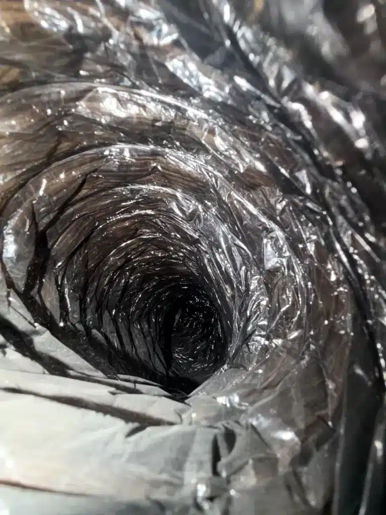 Air duct cleaning: dusty interior of a flexible duct with a wrinkled plastic liner before cleaning
