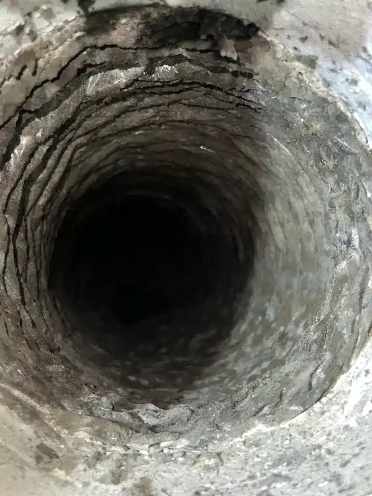 Air duct cleaning: rigid duct interior coated in heavy dust and debris buildup before service