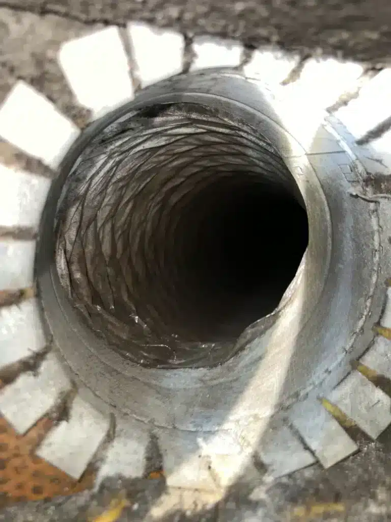 Air duct cleaning: looking into a flex duct line through an opened ceiling boot with grime around the collar