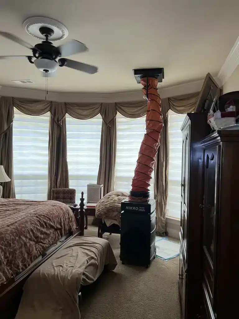 Air duct cleaning in progress: negative air machine with orange hose sealed to a bedroom ceiling vent
