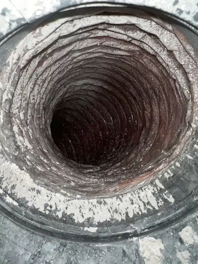 Air duct cleaning before service: thick dust caked along the ridges of a duct interior