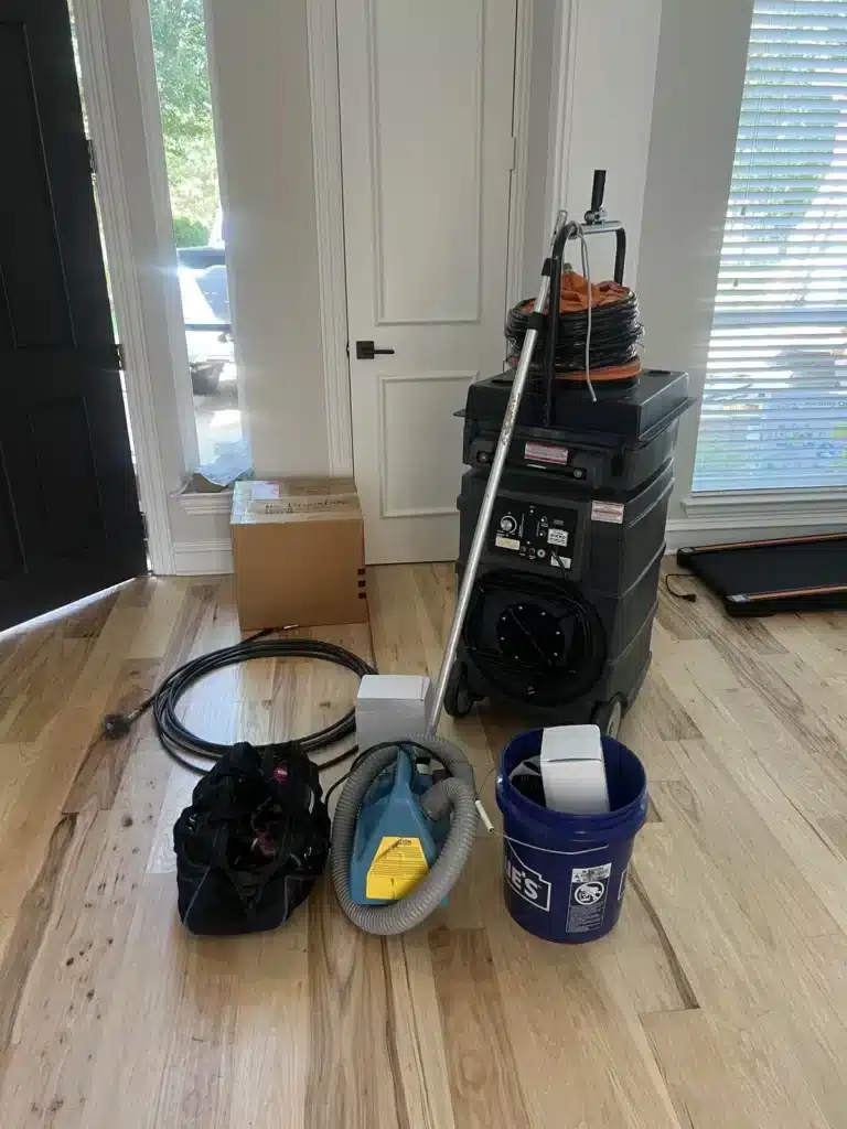 Air duct cleaning equipment staged by the front door: negative air machine, flex hose, hand vacuum and bucket