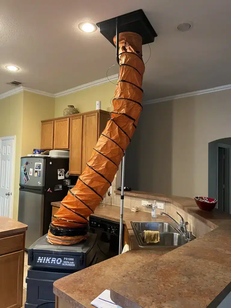 Air duct cleaning in progress: orange flex duct connects a return vent to a negative air machine in a kitchen