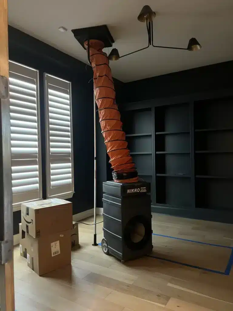 Air duct cleaning underway: flex duct runs from a ceiling vent to a wheeled air scrubber in a home office