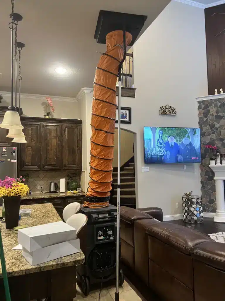 Air duct cleaning in a living area: orange collection duct sealed to a high ceiling return vent