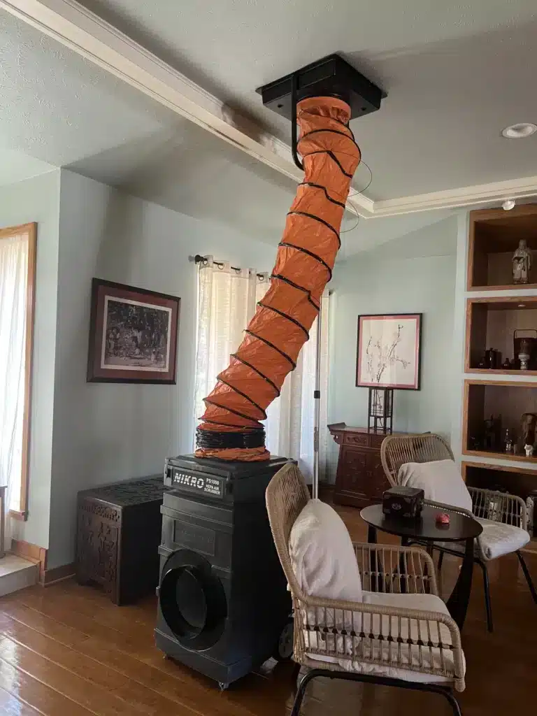 Air duct cleaning setup with flexible orange hose connecting a portable machine to a ceiling vent
