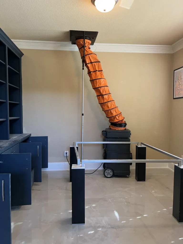 Air duct cleaning: machine and orange hose sealed to a ceiling vent in a room with built-in shelving