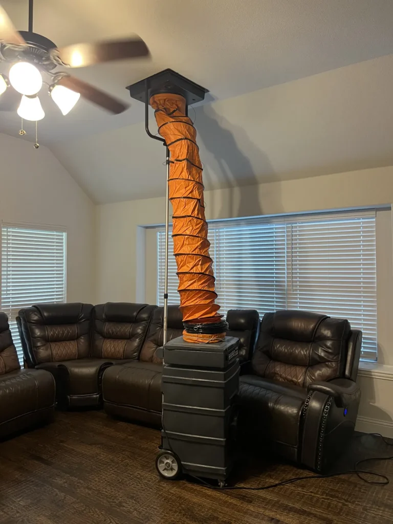 Air duct cleaning: vacuum unit ducted to a ceiling register in a living room with leather sofas