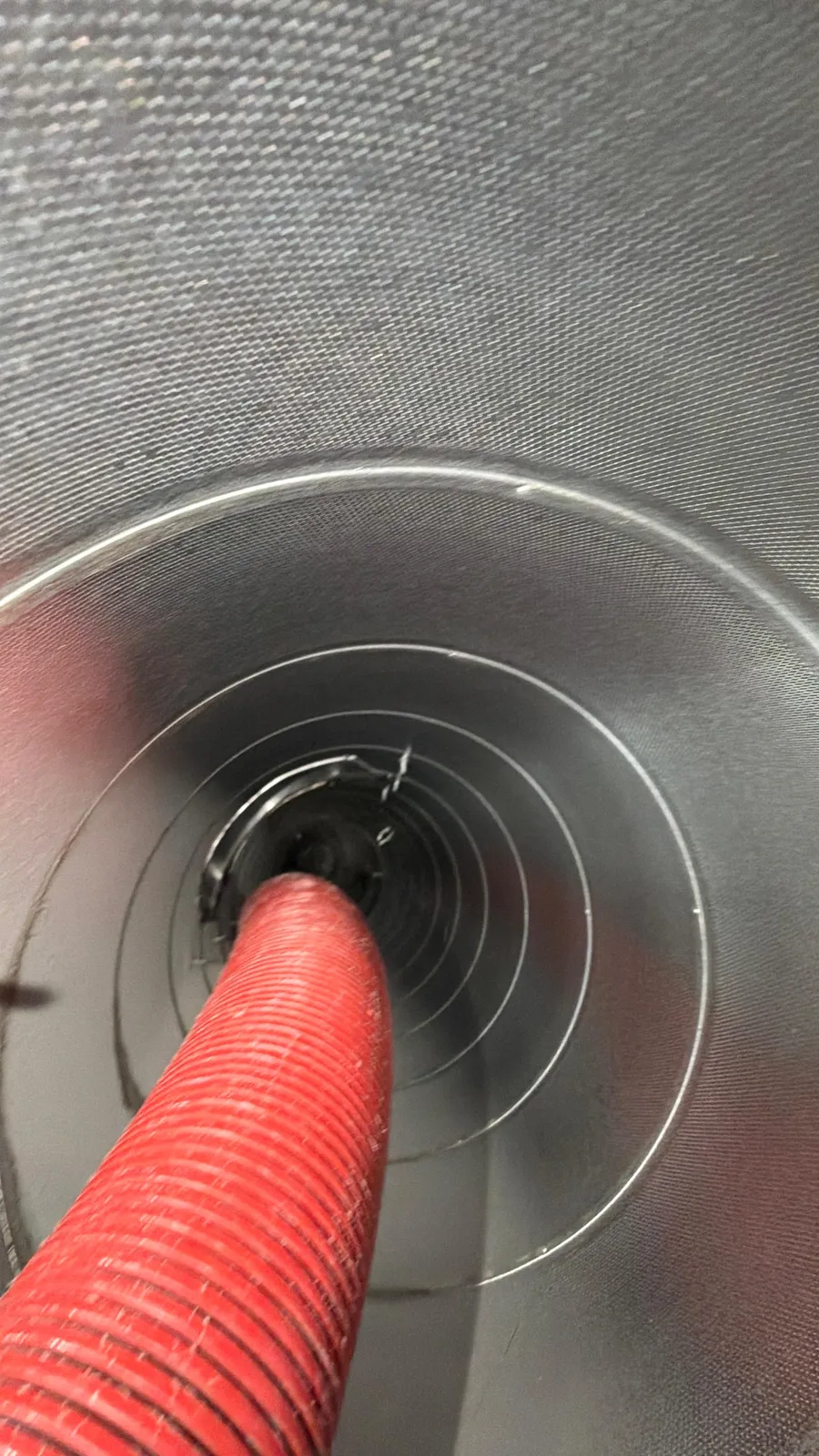Air duct cleaning: red vacuum hose feeding into a round metal duct branch during service