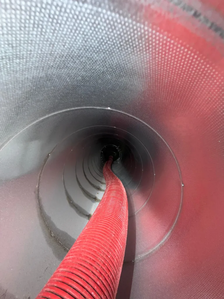 Air duct cleaning: red agitation hose working through a metal duct line to loosen debris