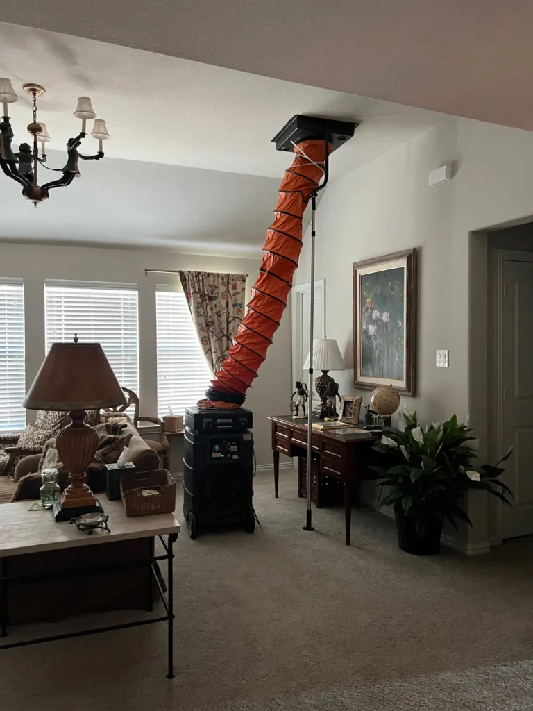 Air duct cleaning: technician reaching a hose into an open ceiling duct beside a return vent