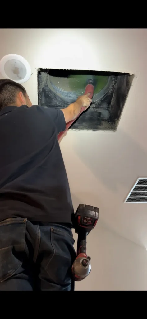 Air duct cleaning: HEPA air scrubber connected by orange duct to a ceiling opening in a dining room