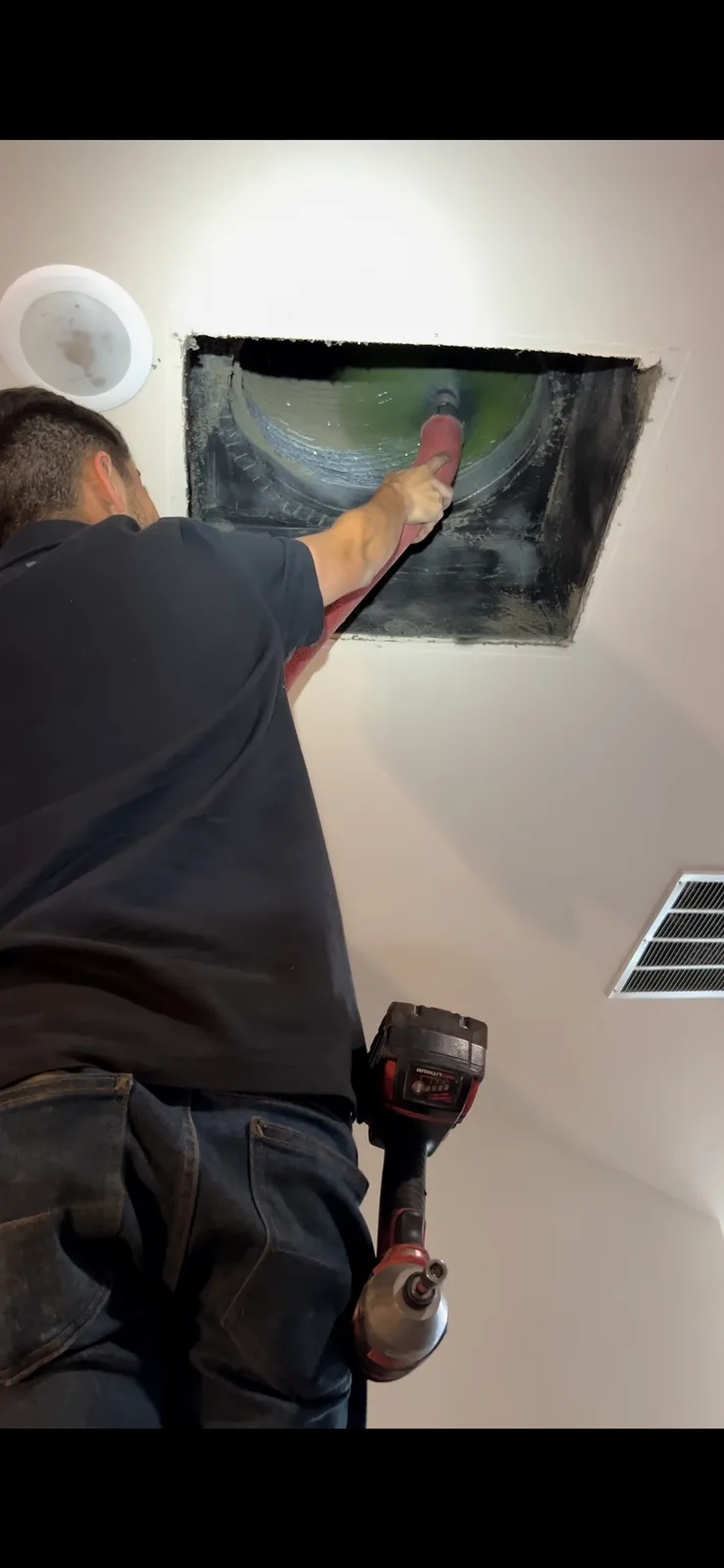 Air duct cleaning: HEPA air scrubber connected by orange duct to a ceiling opening in a dining room
