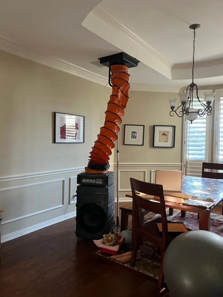 Air duct cleaning setup: portable HEPA unit and orange flex duct running up to the ceiling plenum
