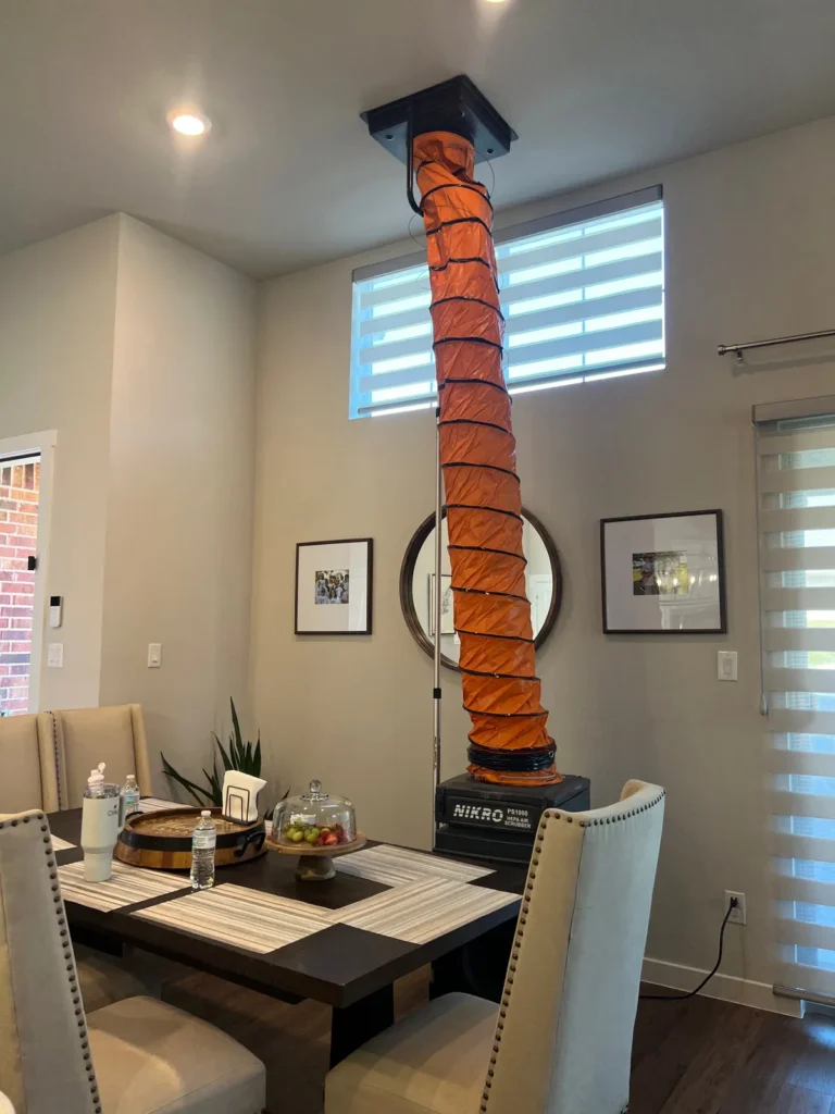 Air duct cleaning: vacuum unit and orange collection hose attached to a ceiling vent above a dining table