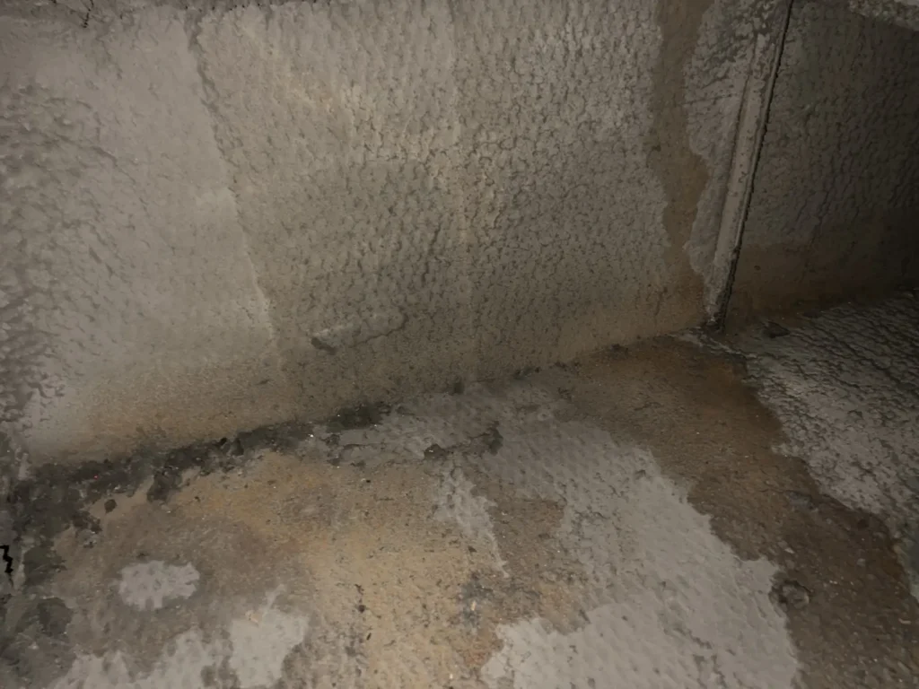 Air duct sanitizing: inside a ductboard trunk showing dust buildup and debris along the seams
