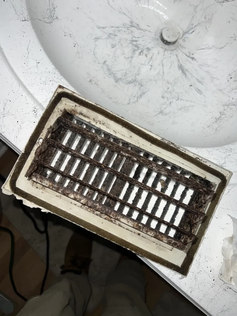 Air duct sanitizing: rusted, dirt-clogged return grille removed for cleaning at a sink