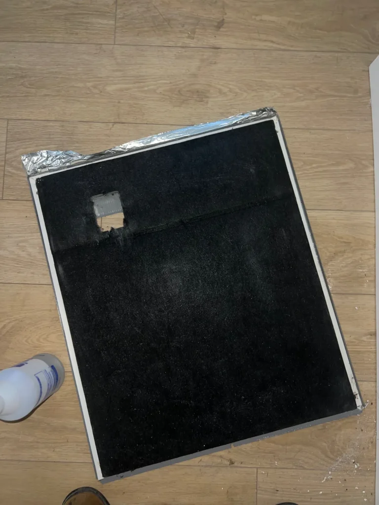 Air duct sanitizing job: removed duct board panel covered in dark buildup, laid on the floor