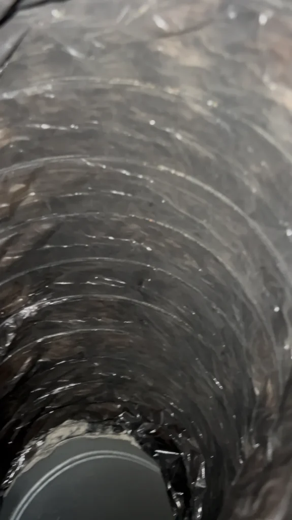Look inside a flexible duct line, dark buildup visible along the inner lining