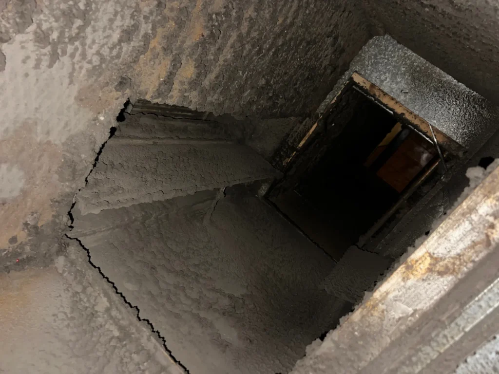 Heavy gray dust caked inside a return air chase before duct cleaning