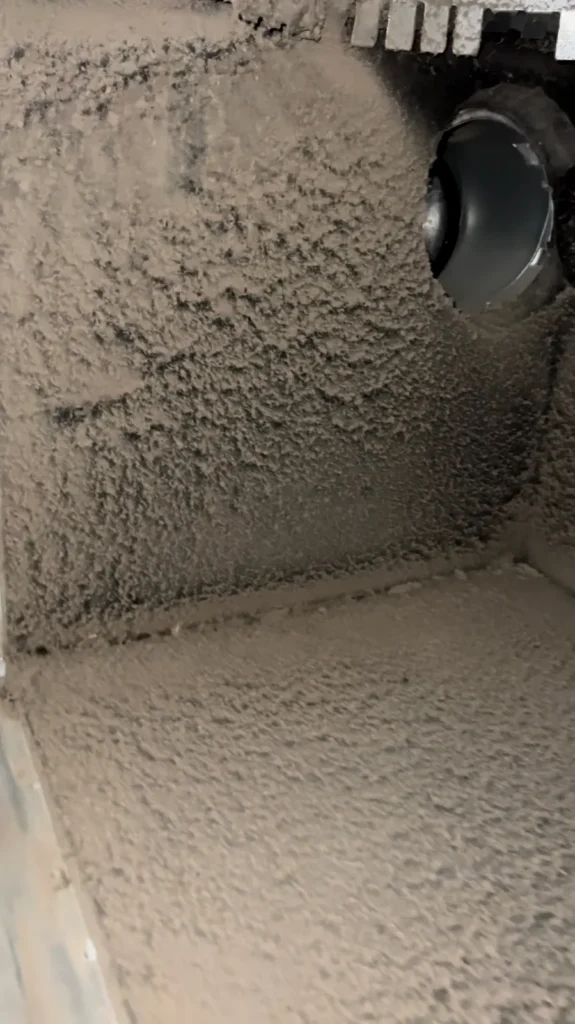 Thick dust blanketing the walls and floor of a plenum around a duct opening