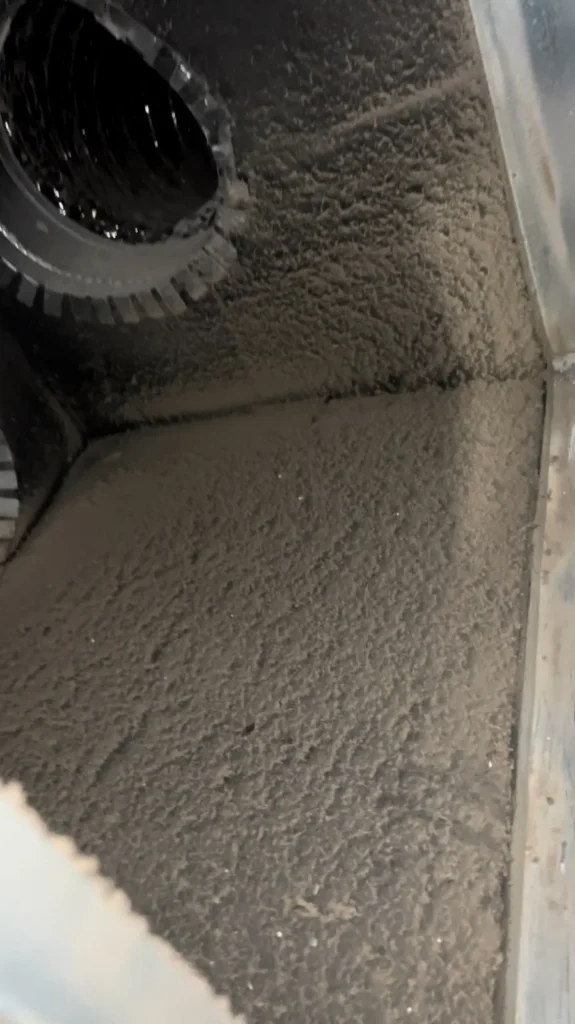 Dust-coated plenum interior with a debris-lined duct collar prior to cleaning