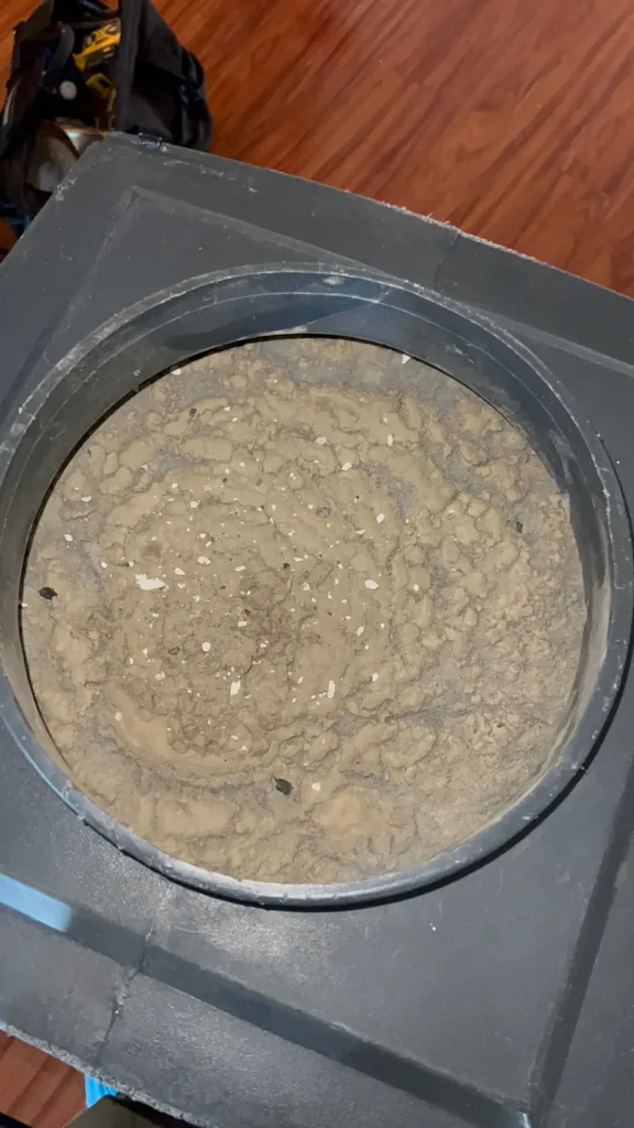 Dense dust and debris packed inside a round floor duct opening before cleaning