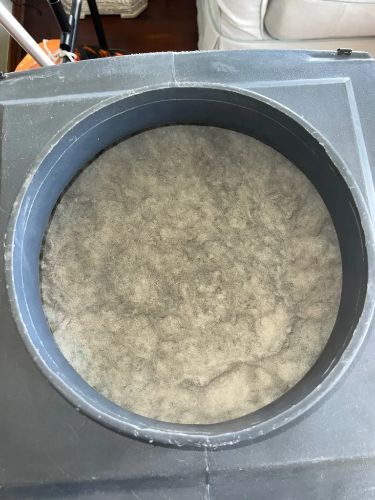 Round duct opening packed solid with gray dust and debris before cleaning