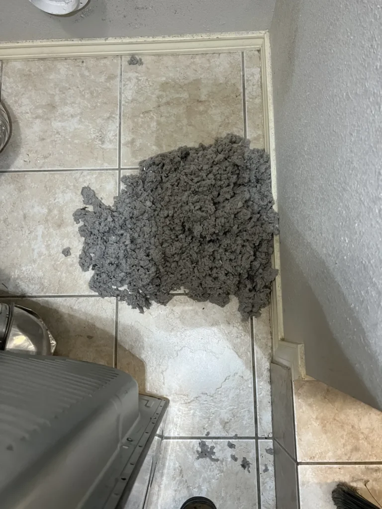 Dryer vent cleaning: thick pile of gray lint pulled from the vent line onto the tile floor