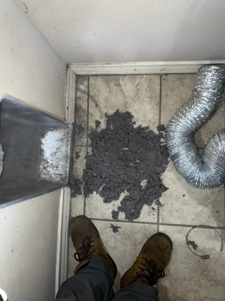 Dryer vent cleaning: technician standing over lint removed from the line, flex duct disconnected nearby