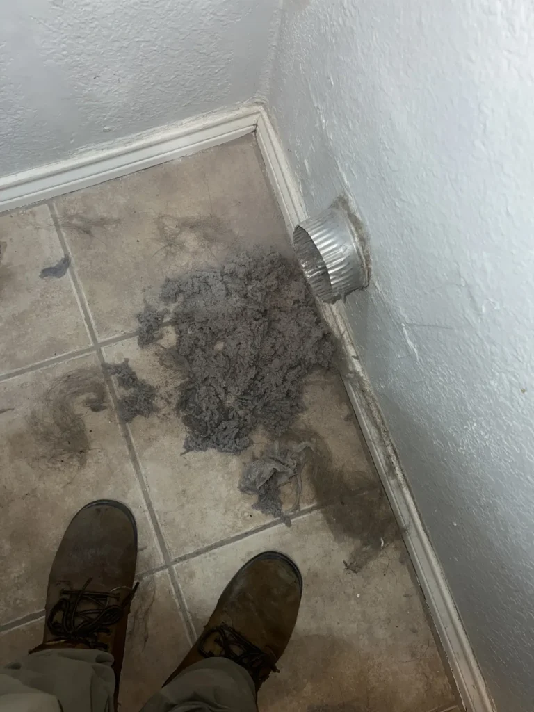 Dryer vent cleaning: lint buildup cleared from a wall vent opening onto the laundry floor