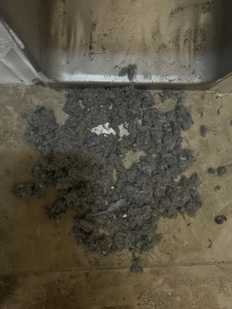 Dryer vent cleaning: clumps of gray lint removed from the vent line beside the dryer