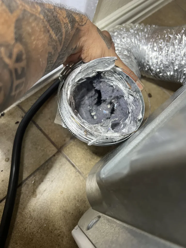 Dryer vent cleaning: technician holding a flex duct end packed with lint behind the dryer