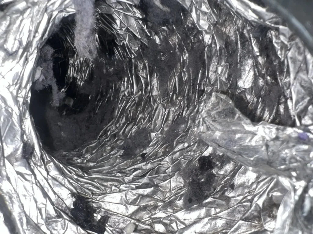 Dryer vent cleaning: inside a foil flex duct coated with dark lint buildup before service