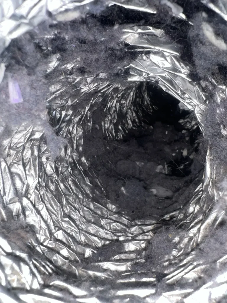 Dryer vent cleaning: looking down a foil flex duct lined with thick gray lint deposits