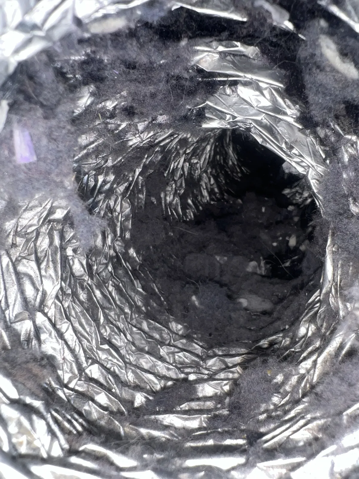 Dryer vent cleaning: looking down a foil flex duct lined with thick gray lint deposits