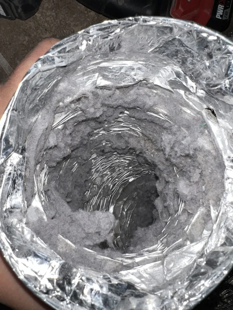 Dryer vent cleaning: technician holding a foil flex duct with lint caked around the opening