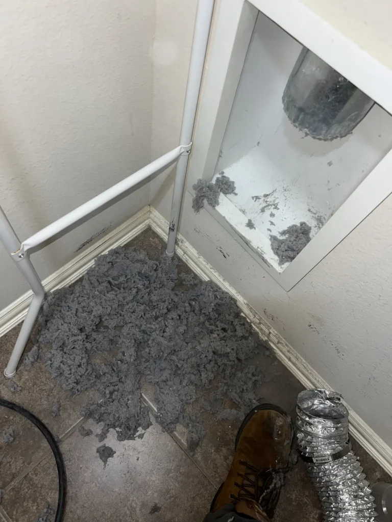 Dryer vent cleaning: lint removed from a wall dryer box, piled on the floor mid-service