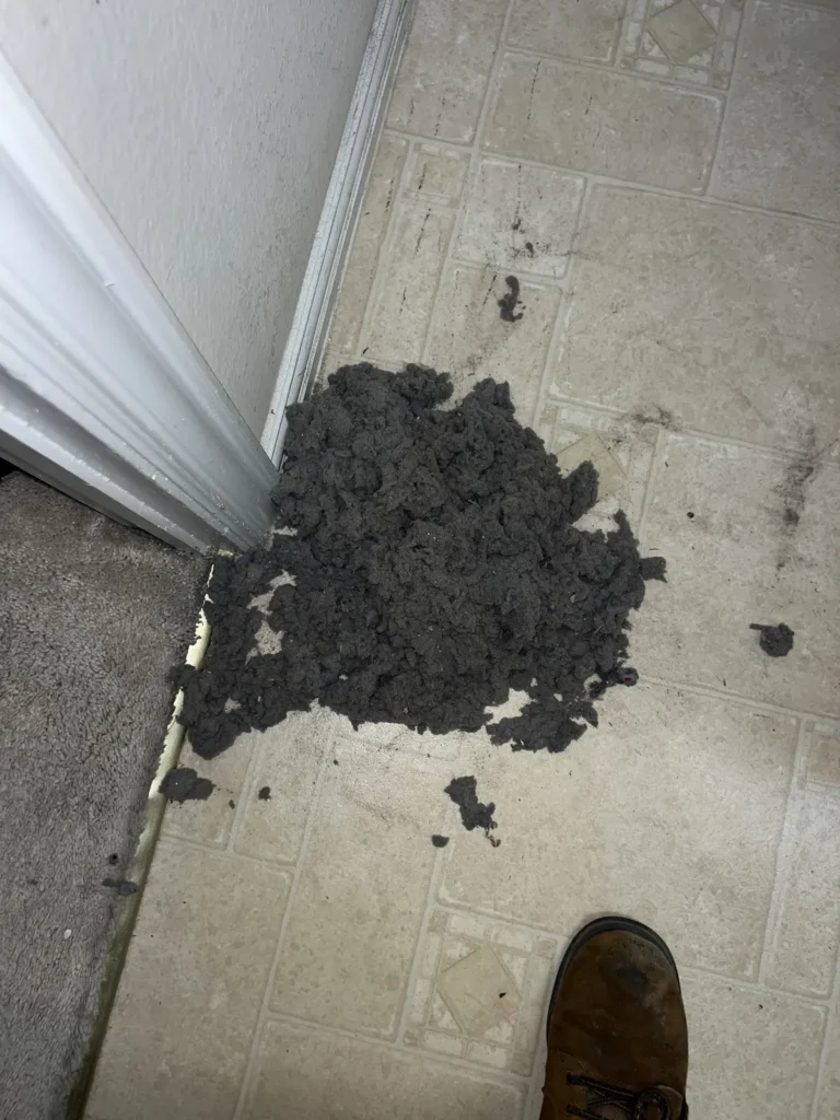 Dryer vent cleaning: pile of gray lint removed from a vent line, gathered on a laundry room tile floor