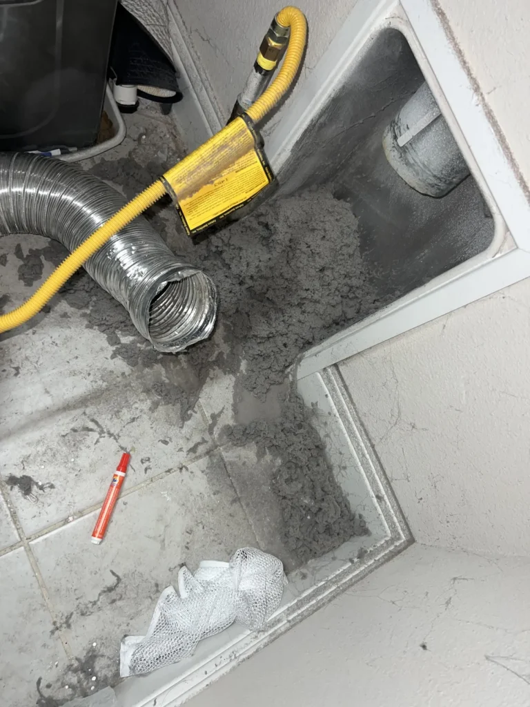Dryer vent cleaning: heavy lint and dust in a dryer alcove, foil transfer duct and gas connector disconnected for service