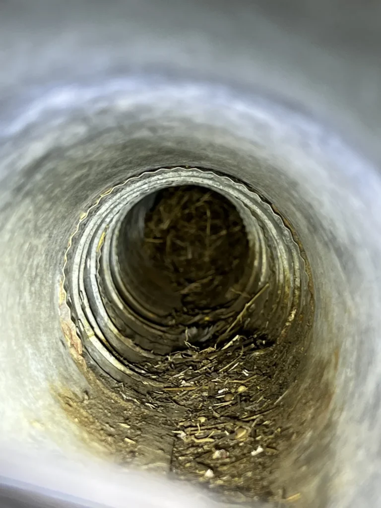 Dryer vent cleaning: inside a metal dryer vent duct showing lint and debris coating the walls before cleaning