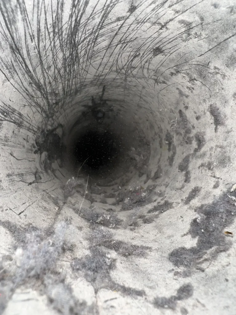 Dryer vent cleaning: looking down a round dryer exhaust duct with lint and dark residue clinging to the walls