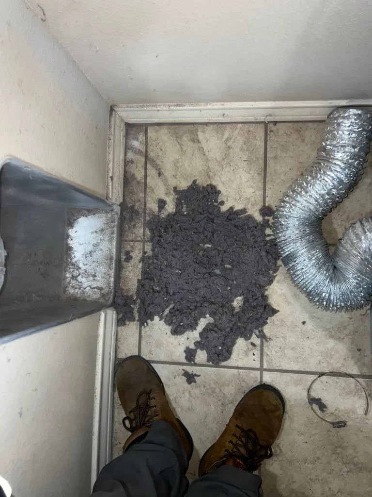 Dryer vent cleaning: technician standing over lint cleared from a wall duct, foil vent hose detached for service