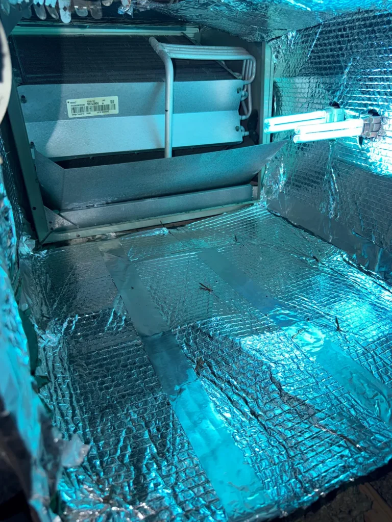 Foil-faced insulation lining a cleaned plenum interior, with a UV lamp visible at the coil